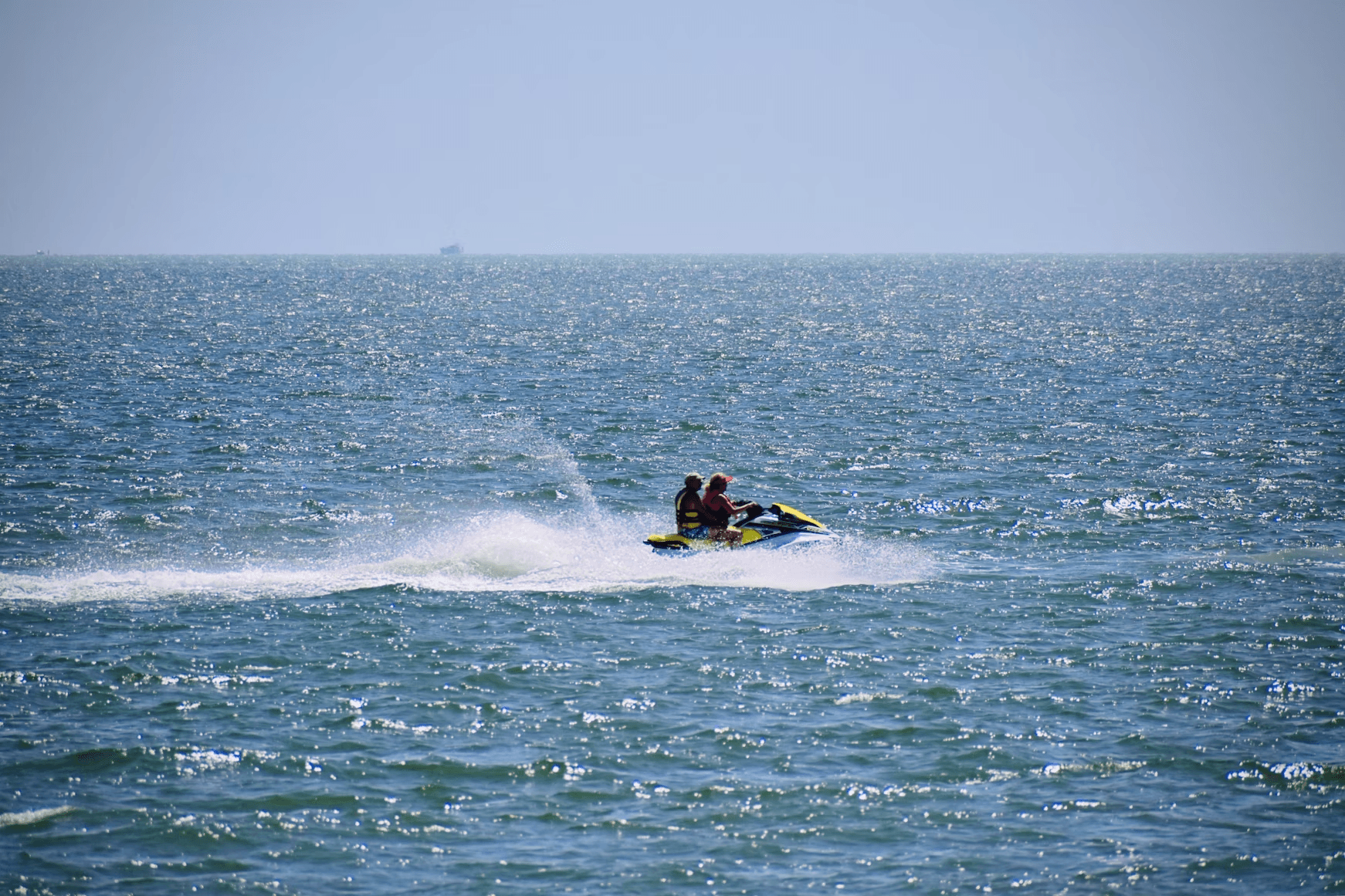 Two riders jet skiing on open ocean near sunny horizon
