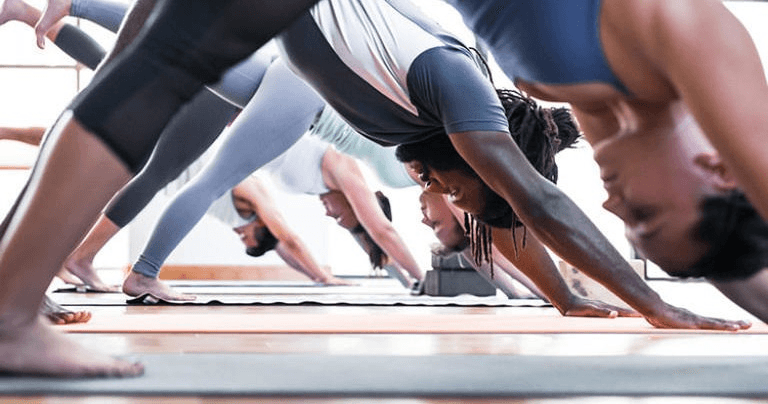 Group practicing downward dog yoga flow in a busy studio