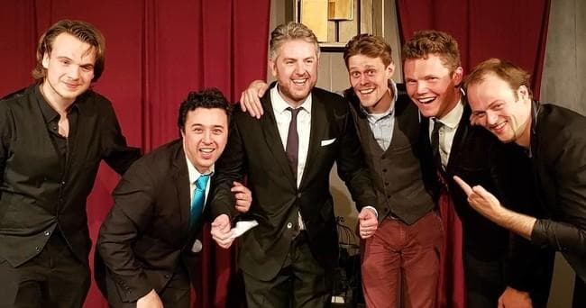 Close-knit magician troupe in formal attire on stage, Amsterdam