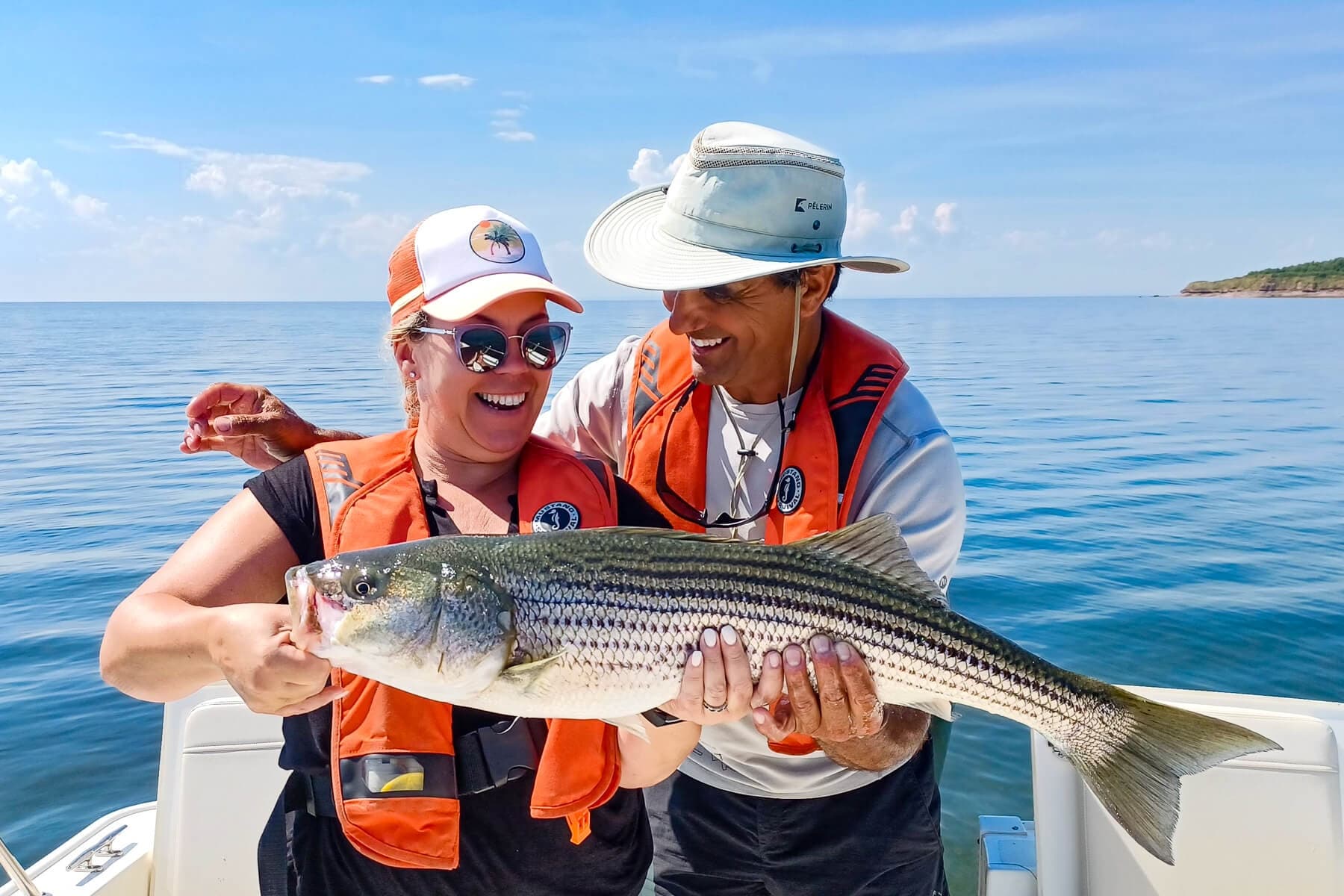 Happy anglers holding striped bass on boat in clear blue sea