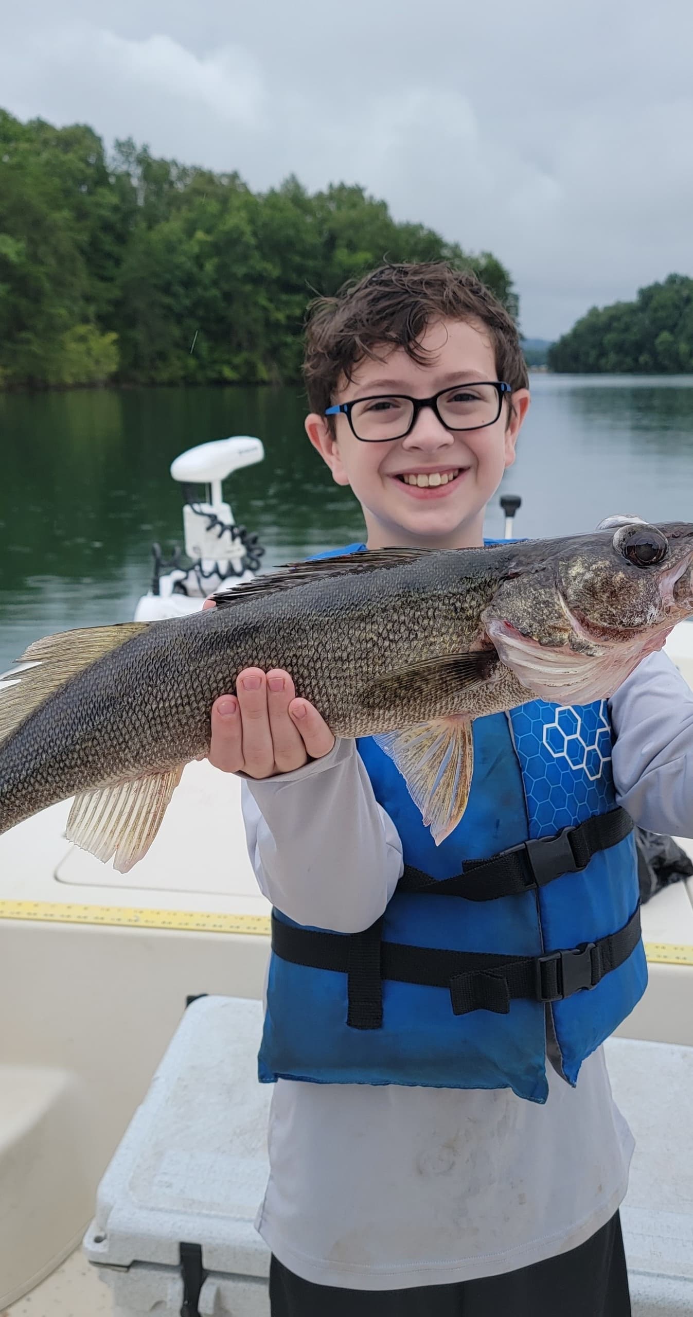 Young angler holding walleye on family boat in calm lake