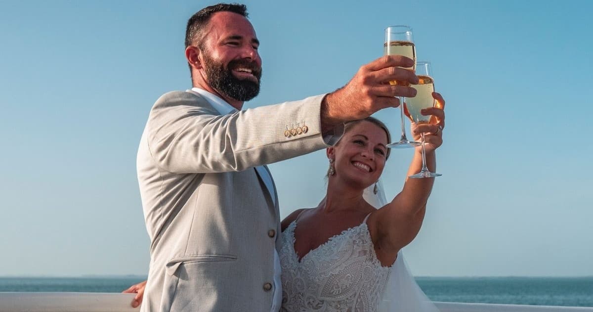 Beach wedding couple toasting at shoreline with ocean backdrop