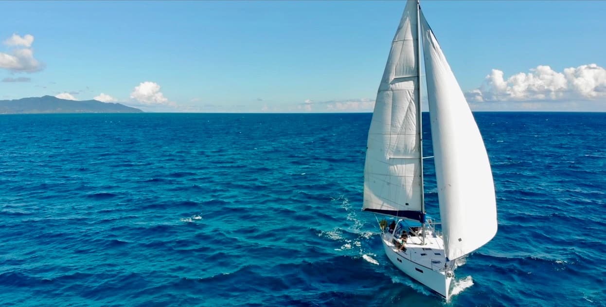 White-sailed yacht cutting across open ocean under blue sky