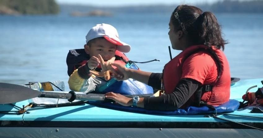 Two kayakers paddling tandem on calm coastal waters near shore