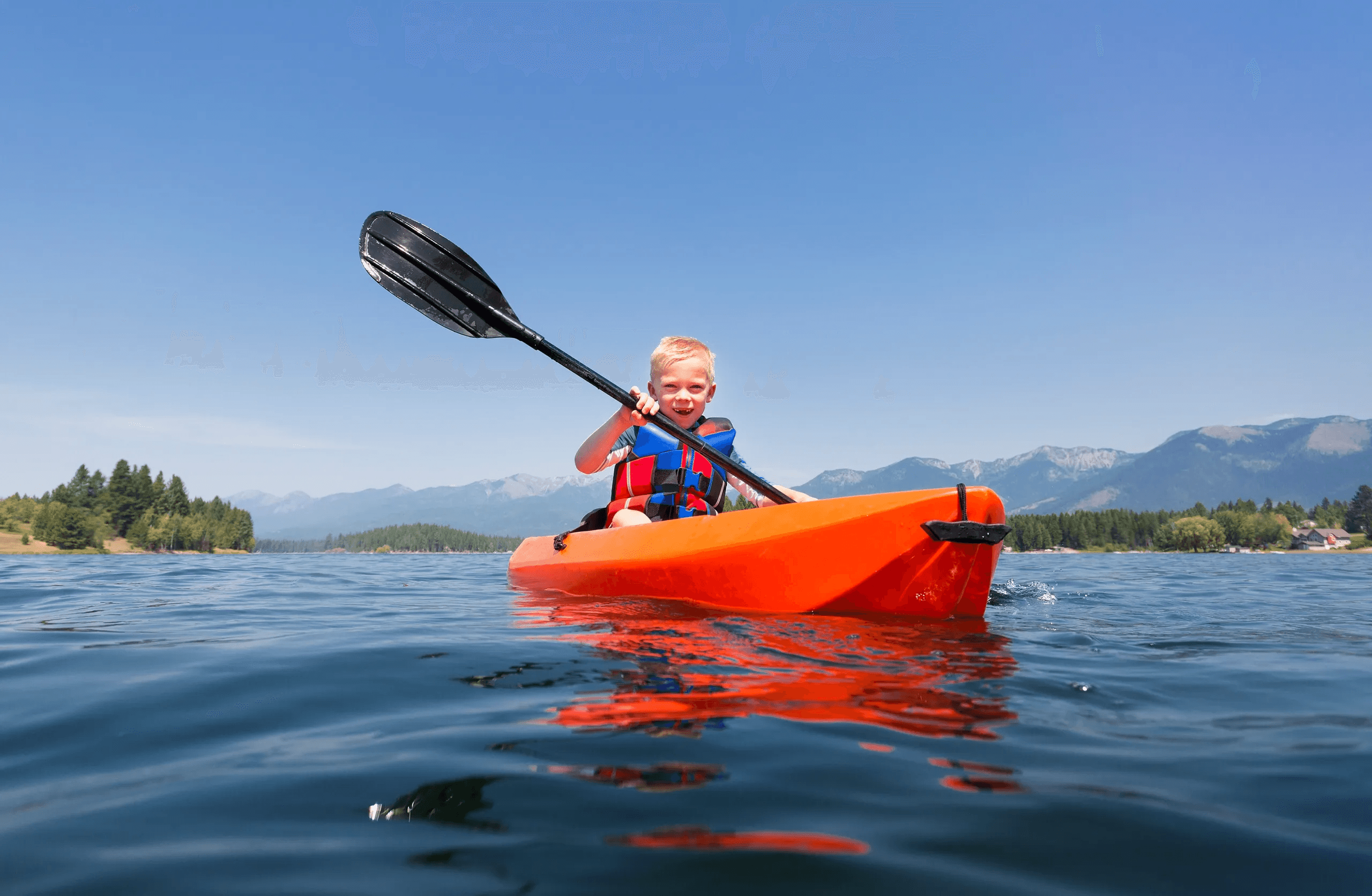 Solo kayaker paddling bright red kayak on clear mountain lake