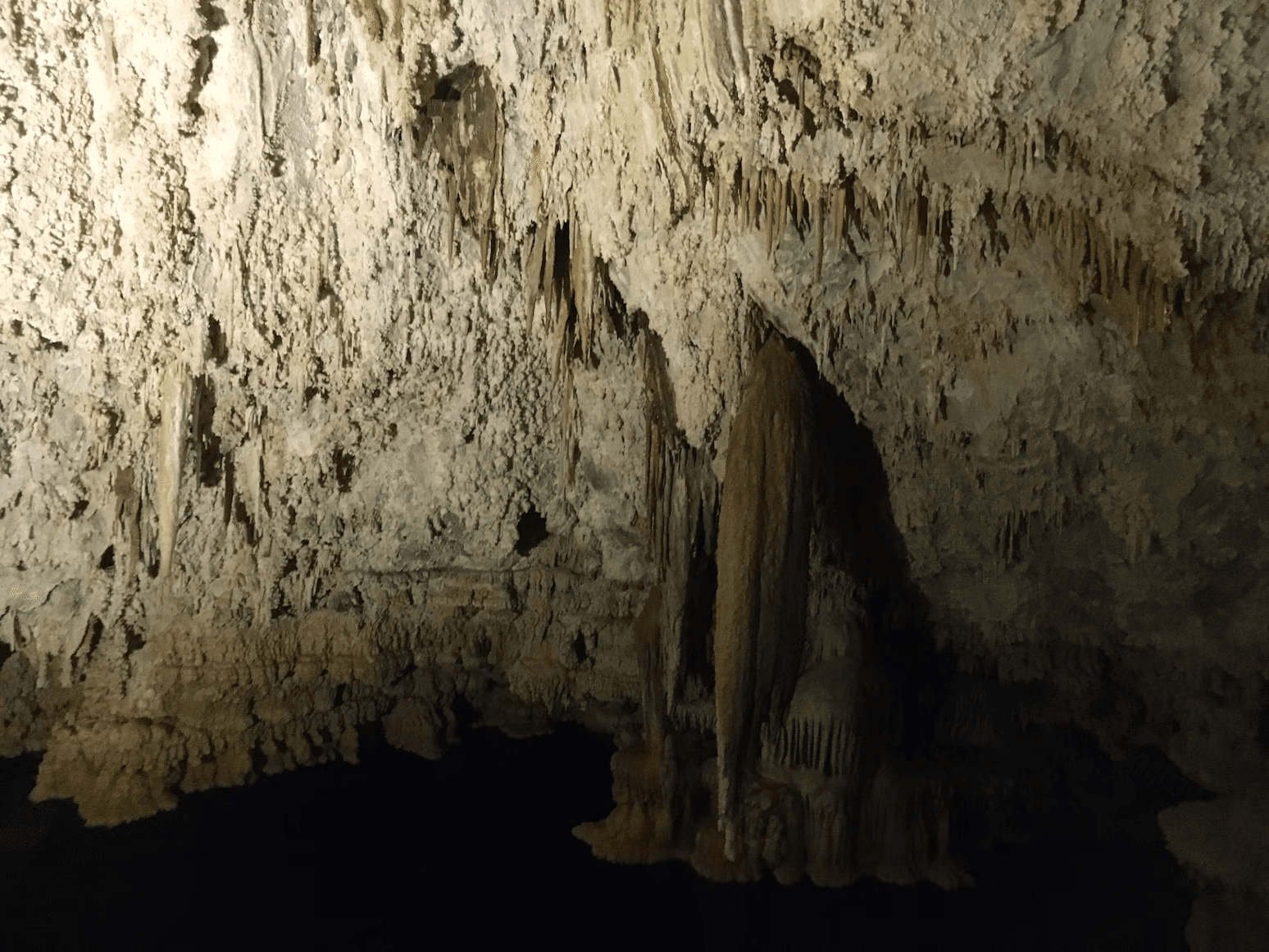 Large central speleothem and reflection in a dim cave chamber