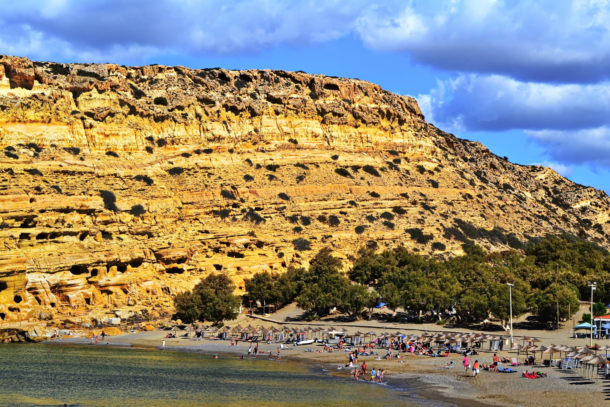 Dramatic sandstone cliff overlooking crowded sandy beach cove