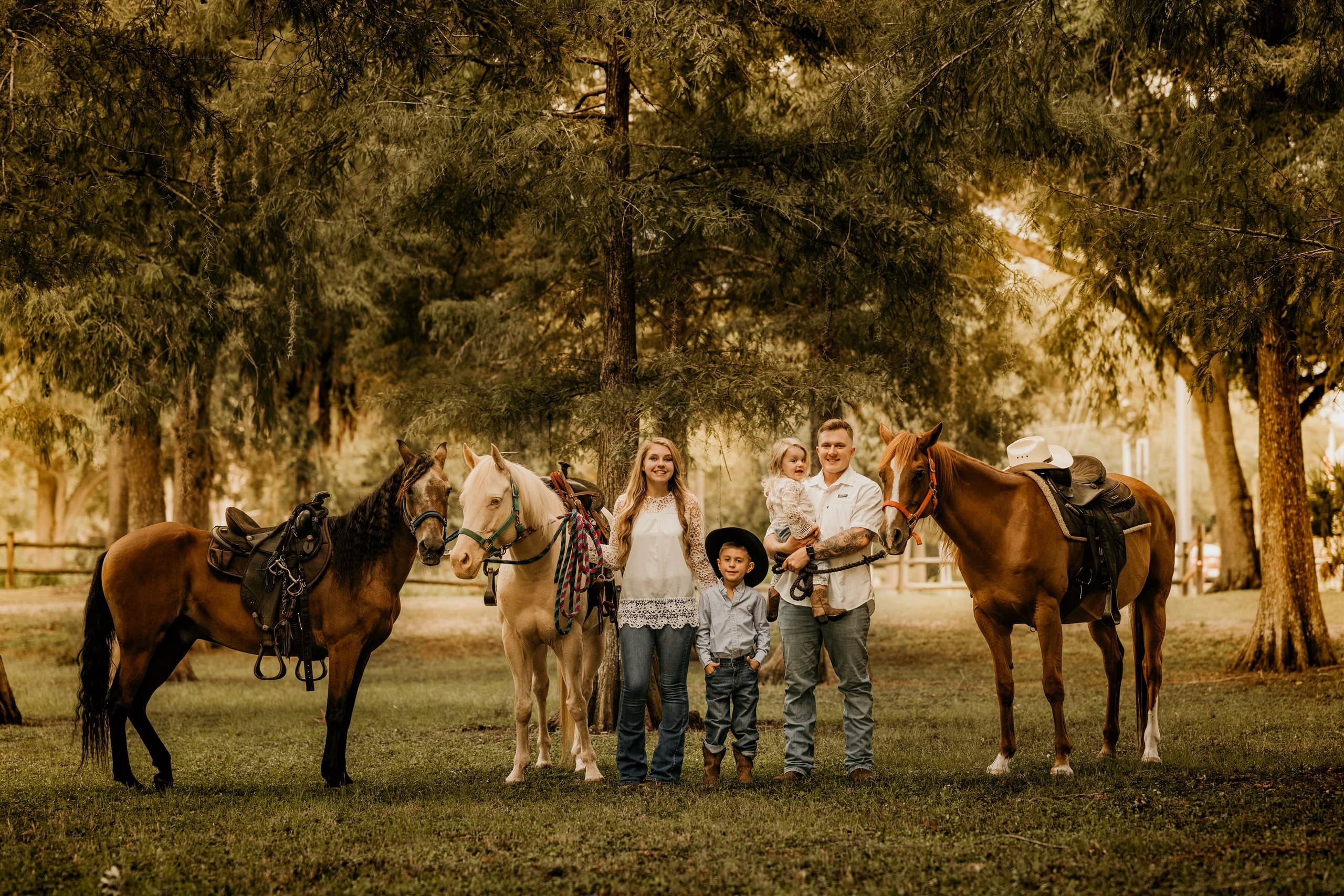 Family posing with ranch horses in shaded oak pasture