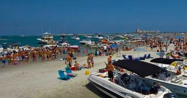Busy sandbar and anchored boats with beachgoers in shallow gulf