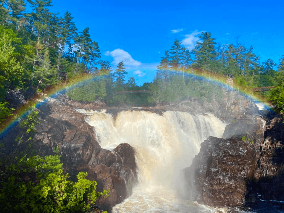 Rainbow arcing over waterfall in lush forest river gorge