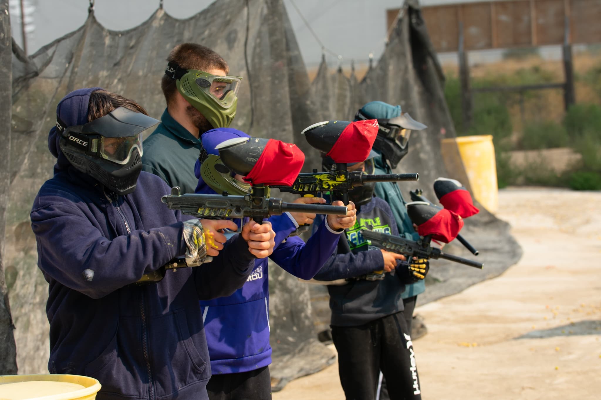 Group of masked paintball players aiming markers on outdoor field