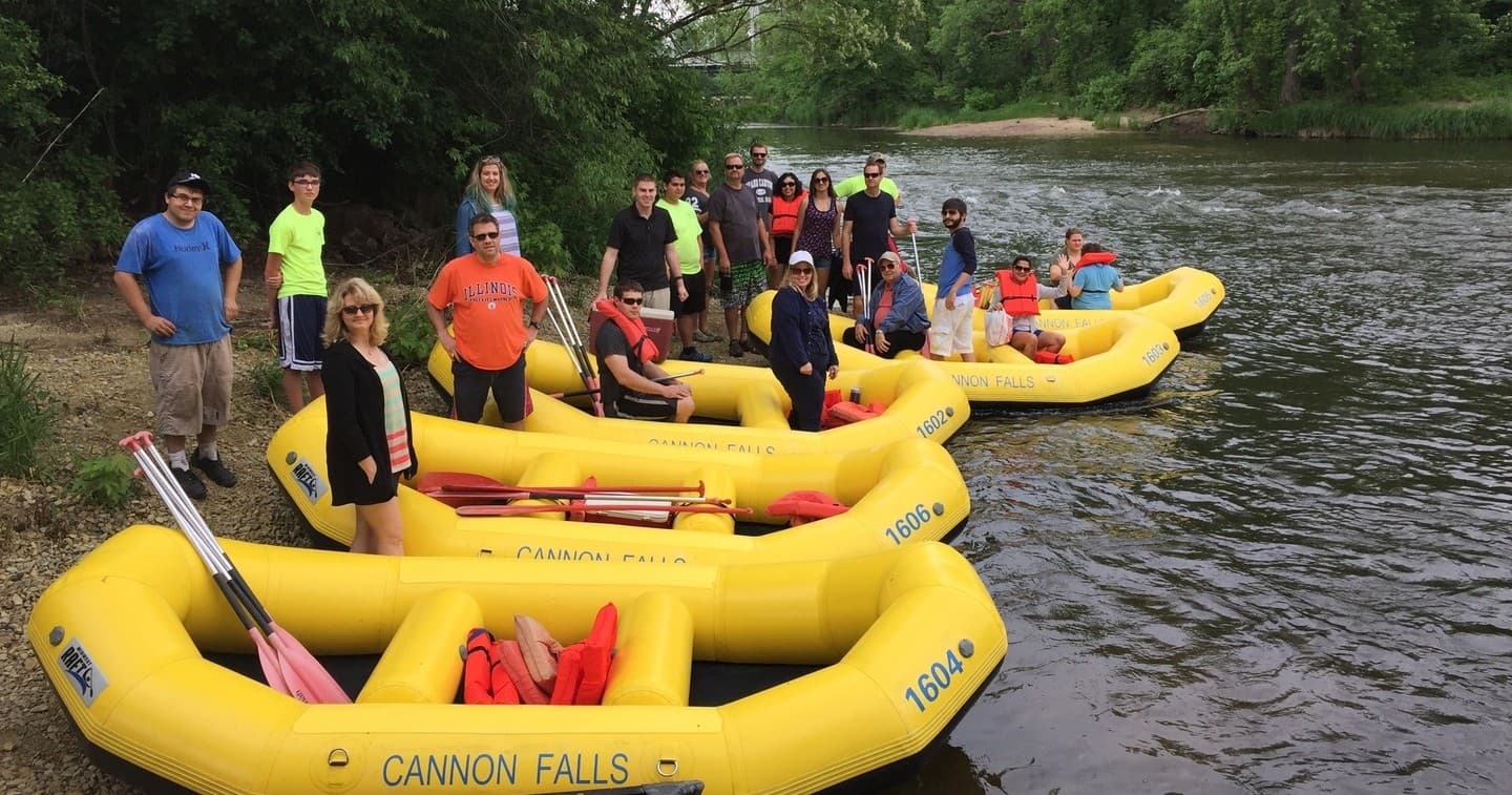 Group of yellow whitewater rafts with paddlers on riverbank