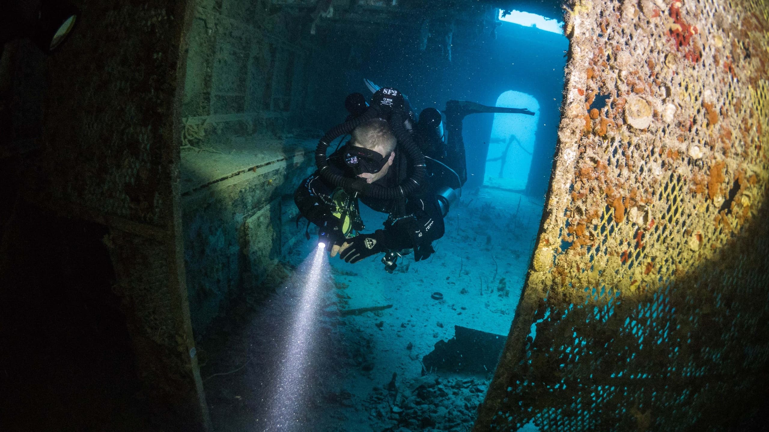 Diver exploring shipwreck interior with flashlight underwater