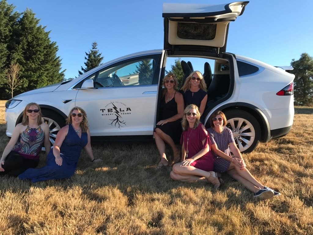 Small group enjoying outdoor winery tour beside Tesla Model X