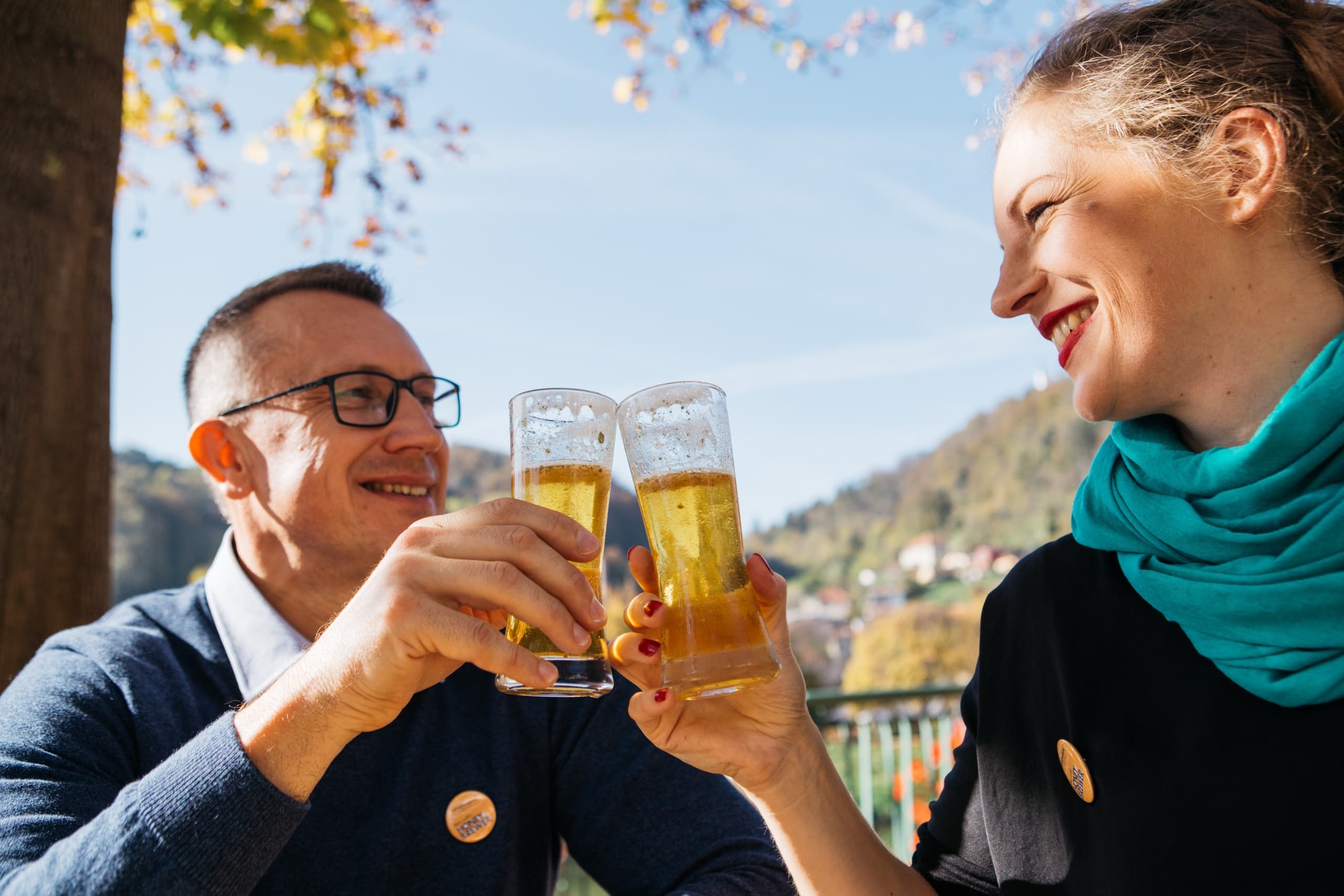 Friends clinking beer glasses outdoors at sunny terrace