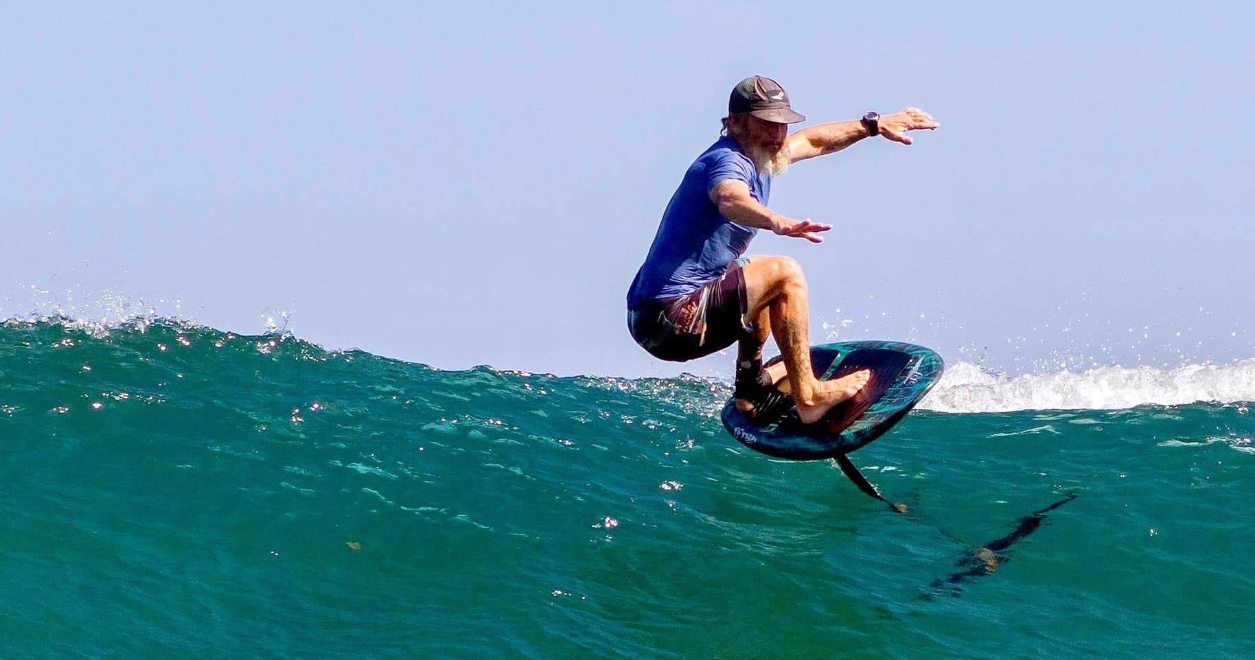 Surfer hydrofoiling over breaking wave on clear ocean swell