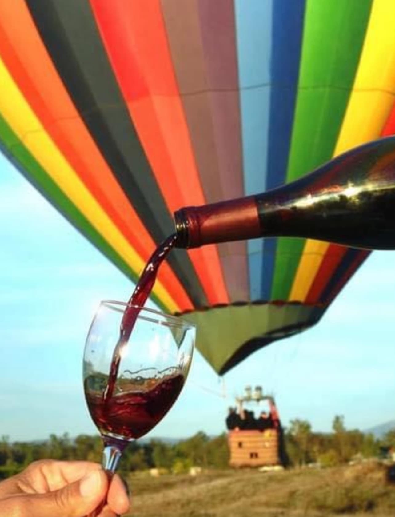 Pouring red wine in foreground with colorful hot air balloon flight