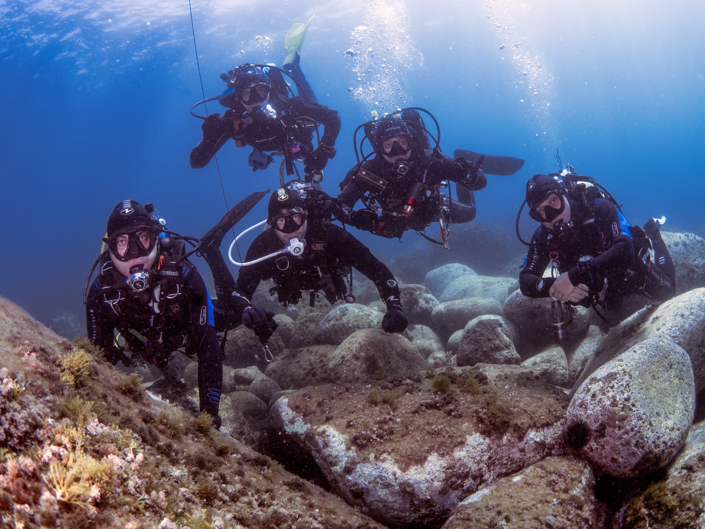 Group scuba divers surveying rocky reef in shallow clear water