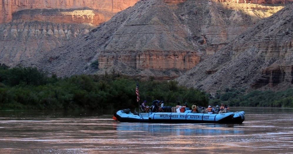Panoramic river raft cruising past desert canyon walls at dusk