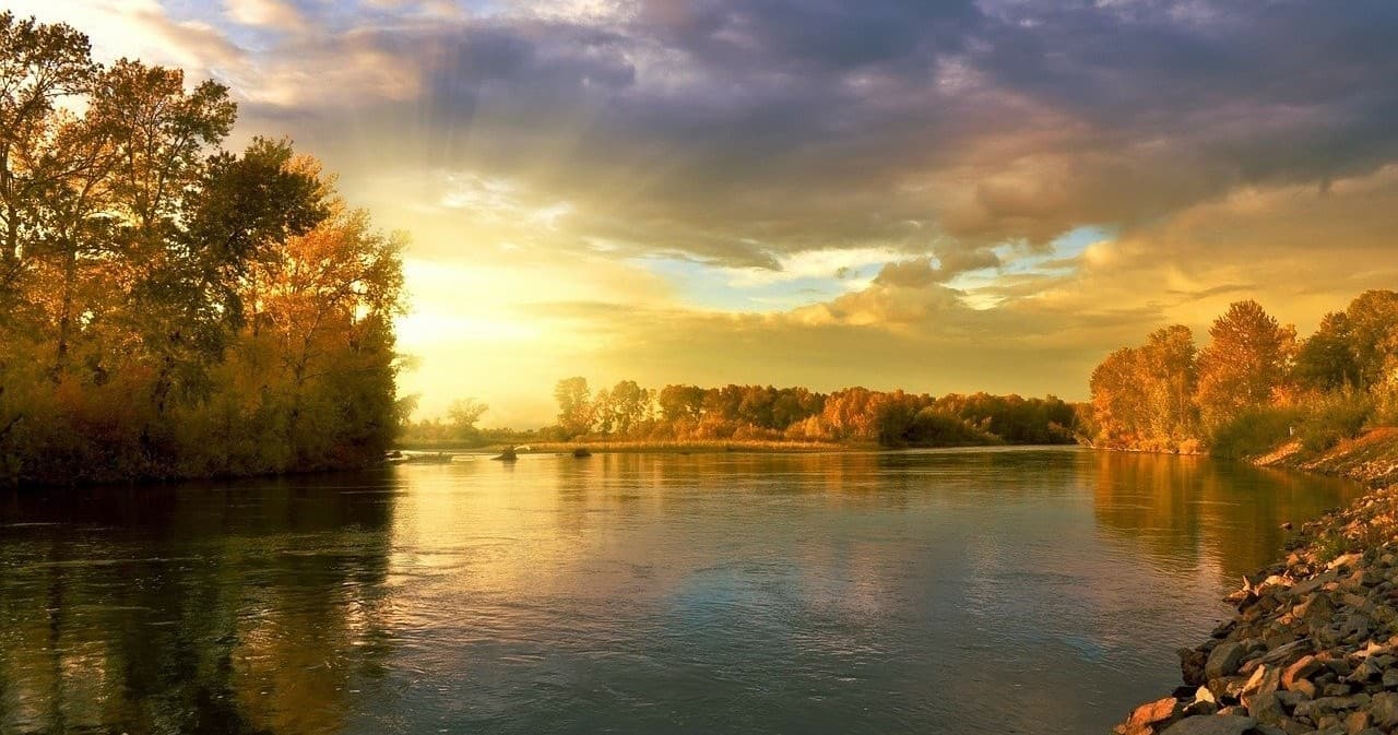 Canoeing on tranquil tree-lined river at sunset