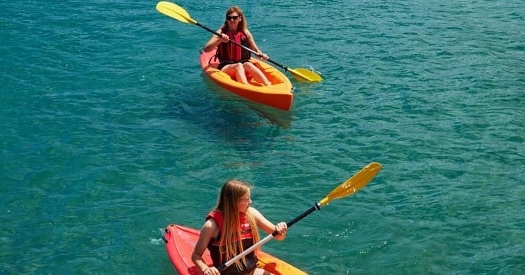Aerial view of two kayakers paddling on clear emerald water
