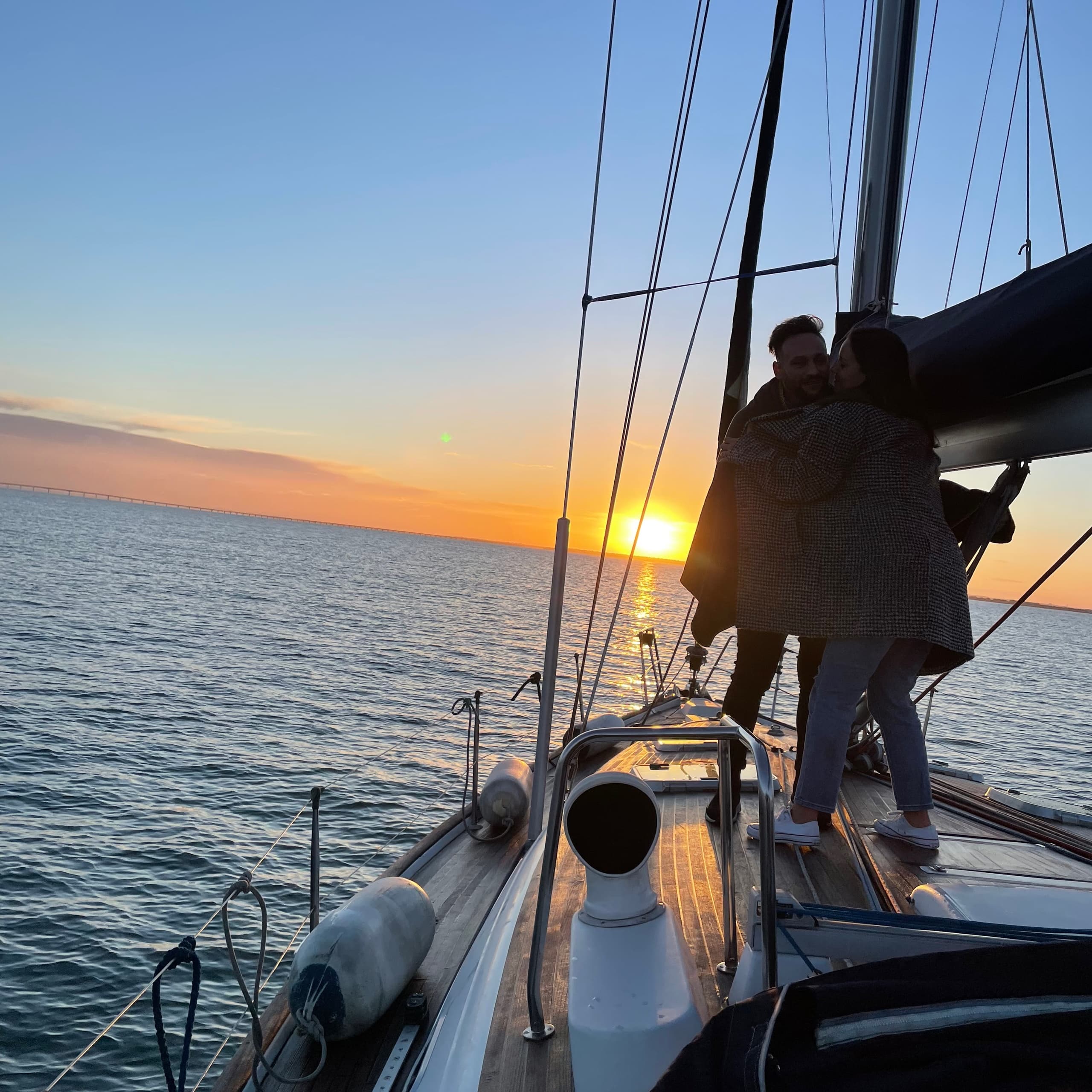 Couple on bow of sailboat at sunset over open water
