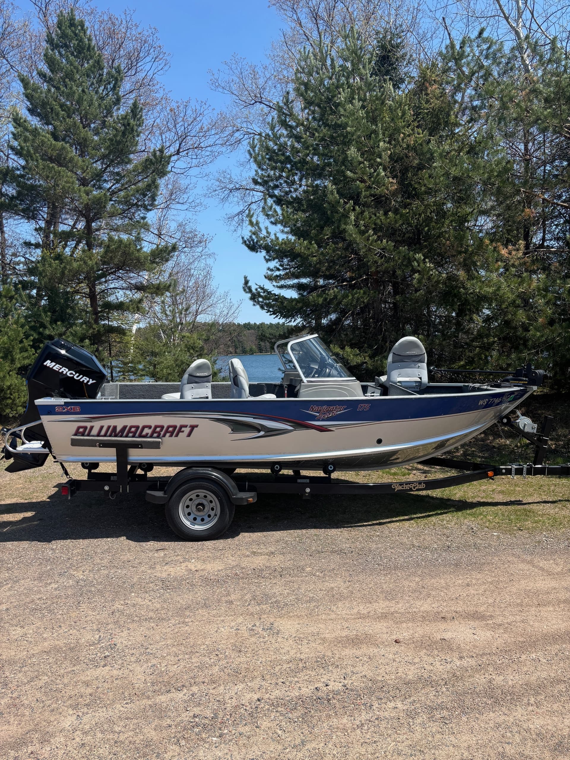 Alumacraft fishing boat parked on trailer by pine trees