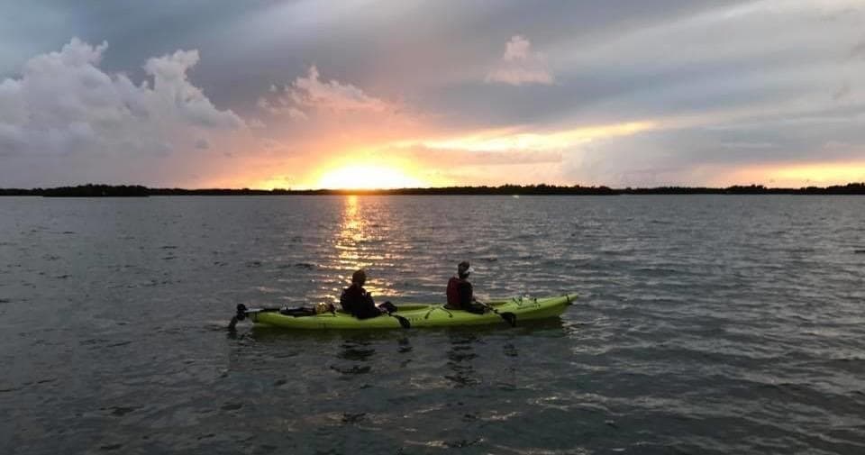 Two kayakers silhouetted paddling at sunset on open water