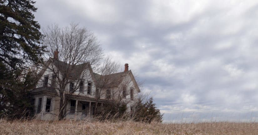 Abandoned farmhouse on windswept field under cloudy sky