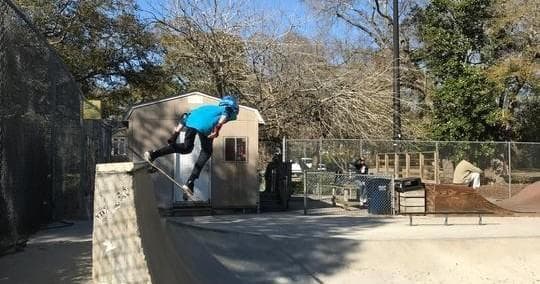 Skateboarder carving high on vert ramp in sunny outdoor community skatepark