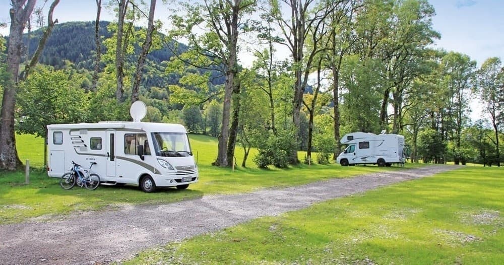 Motorhome at scenic green campsite with trees and hills