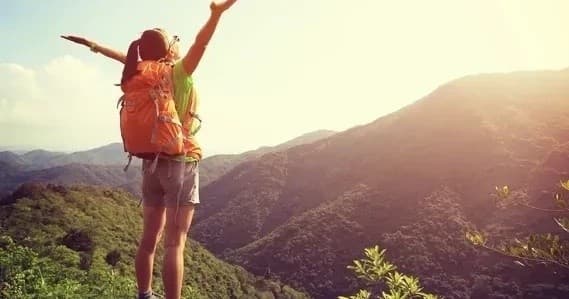 Hiker with backpack celebrating sunrise on mountain ridge