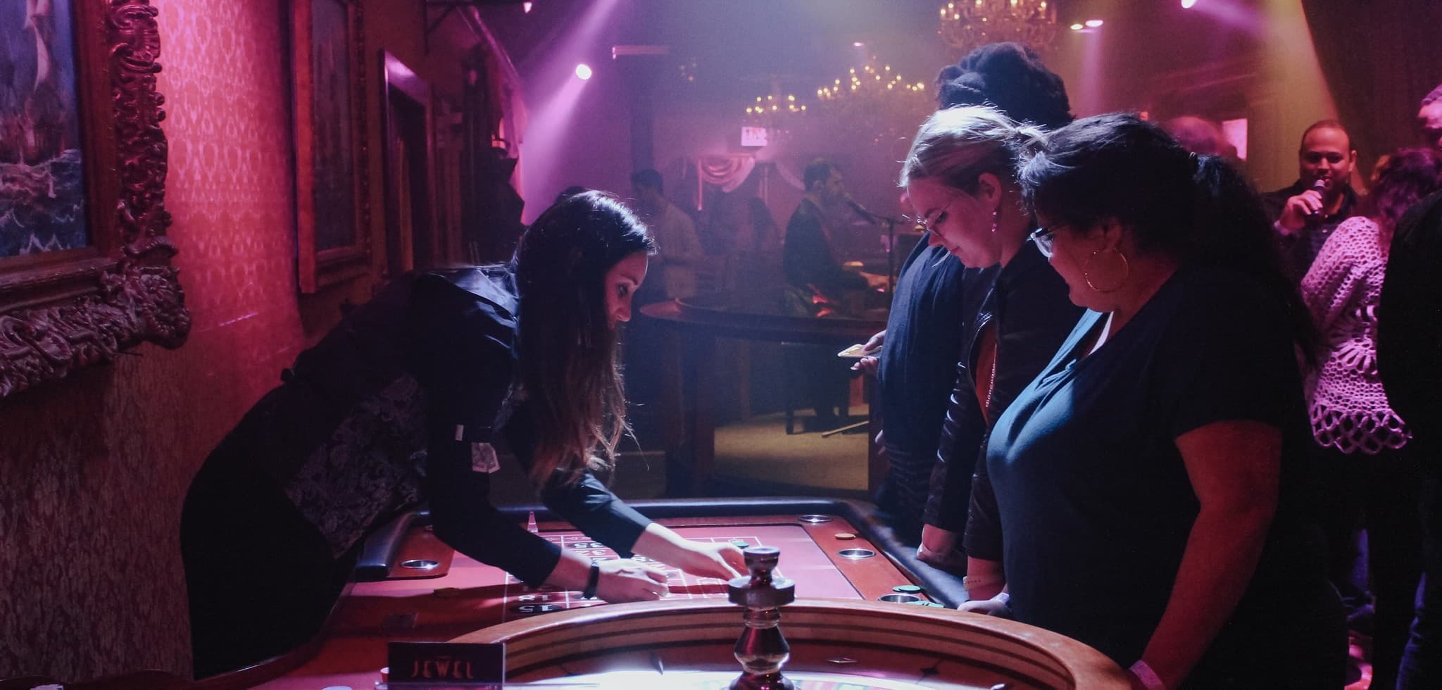Players gathered around roulette table in dim nightclub casino