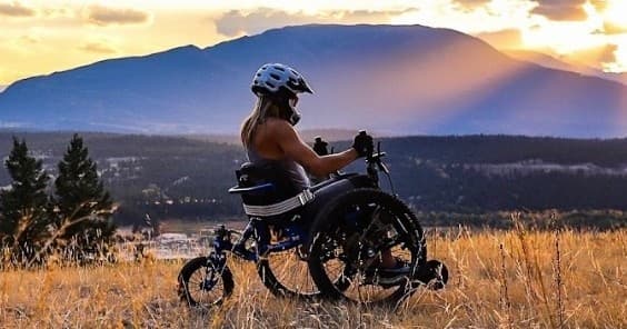 Adaptive handcycle rider overlooking mountain sunset on grassy ridge