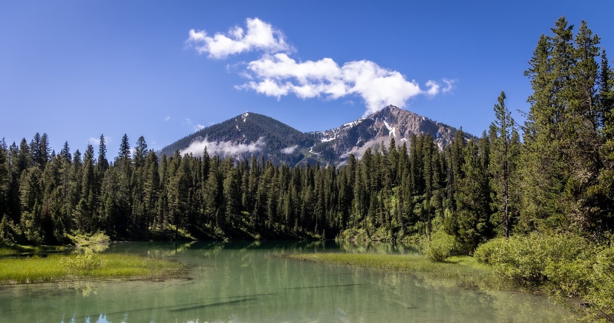 Alpine mountain lake reflecting peaks near forested campsite