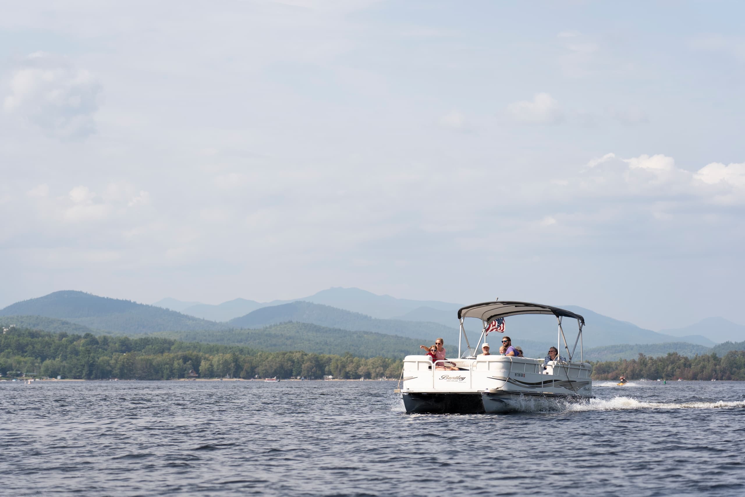 Pontoon boat cruising on Schroon Lake with mountain backdrop