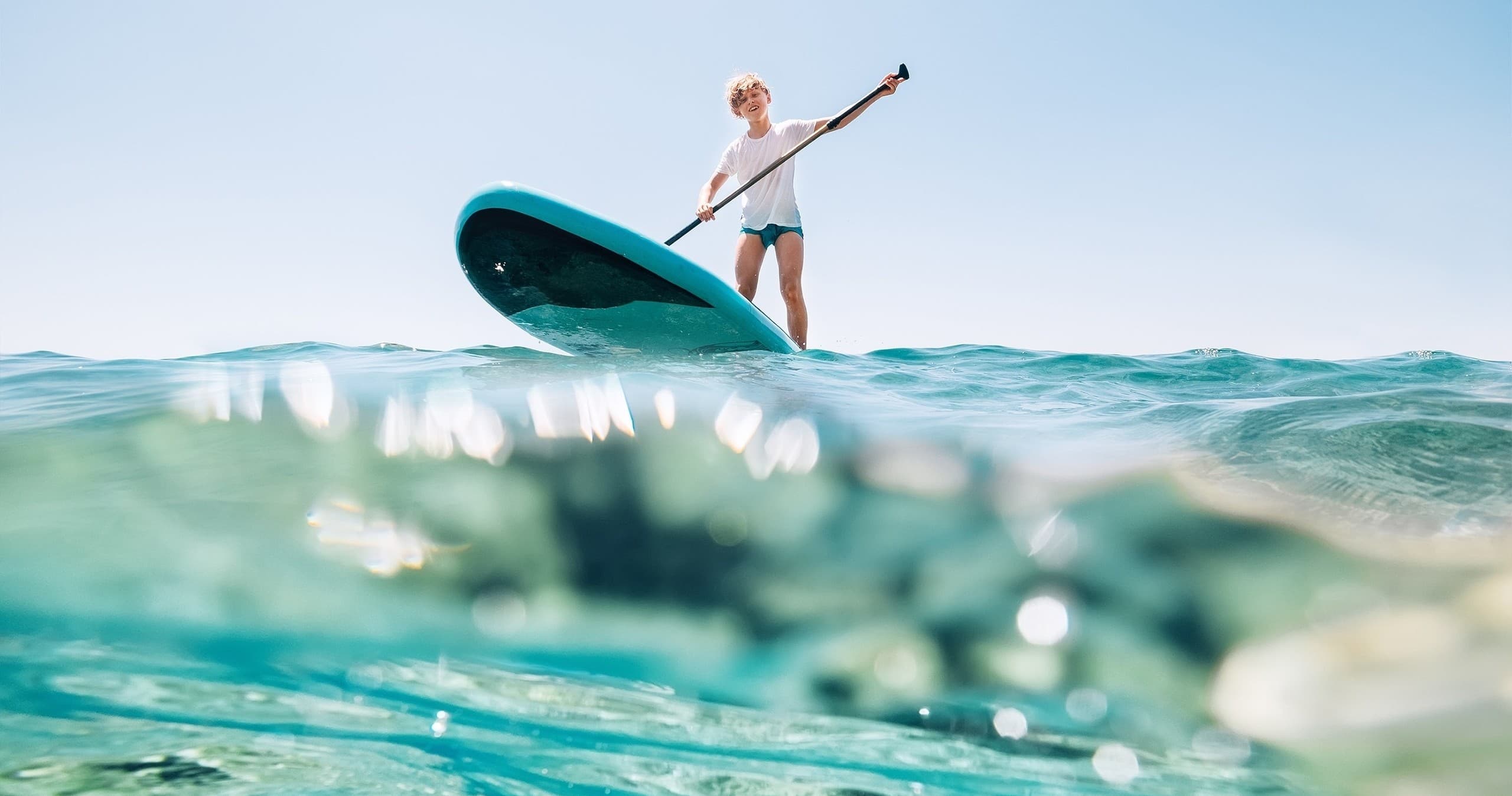 Stand-up paddleboarder on turquoise ocean with low wave
