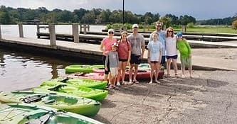 Group of campers with kayaks on shore at launch ramp