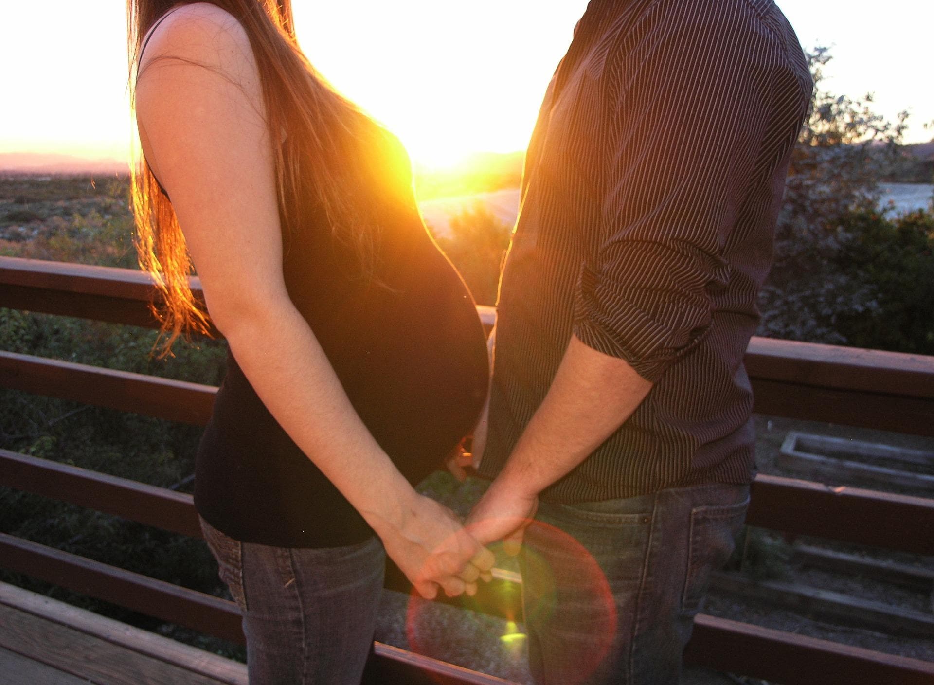 Pregnant couple holding hands at sunset on outdoor deck