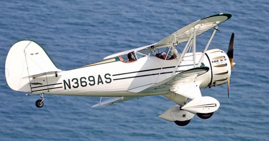 White vintage biplane performing scenic flight over blue ocean