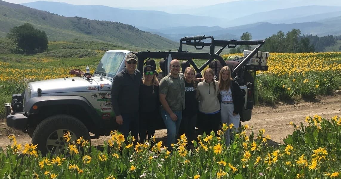 Off-road jeep tour group among alpine wildflower fields and hills