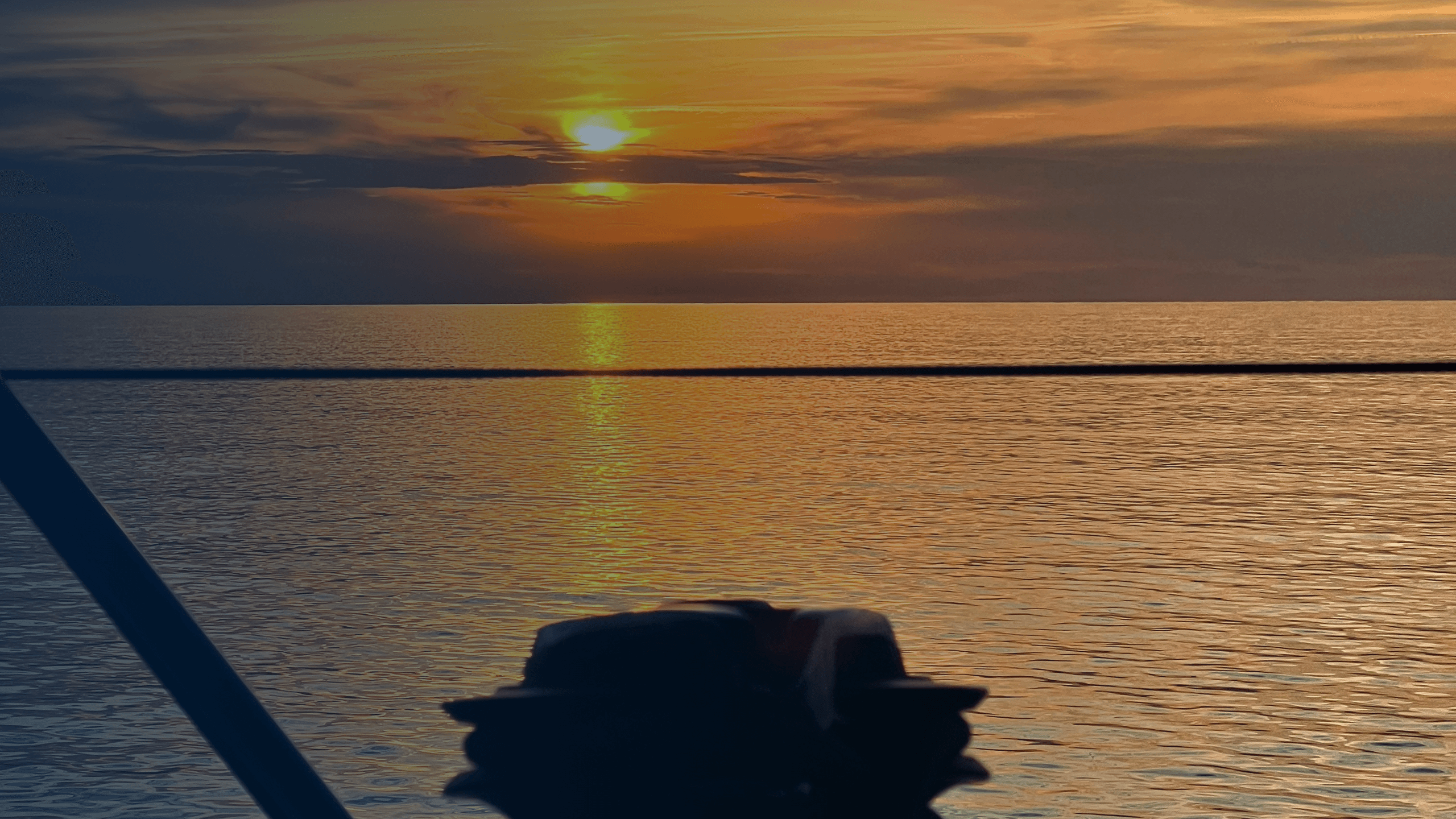 Sailboat silhouetted at sunset on calm open sea