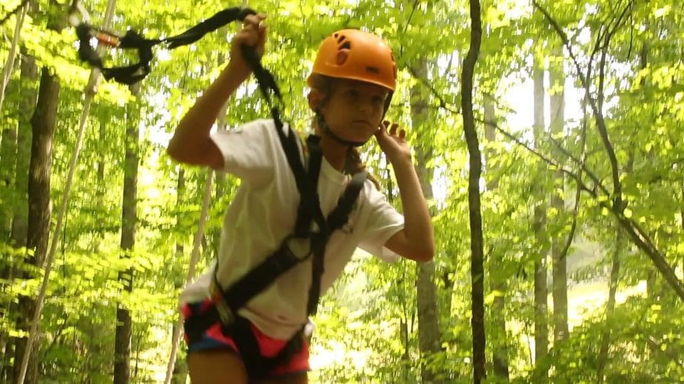 Child ziplining through sunlit forest canopy on harness
