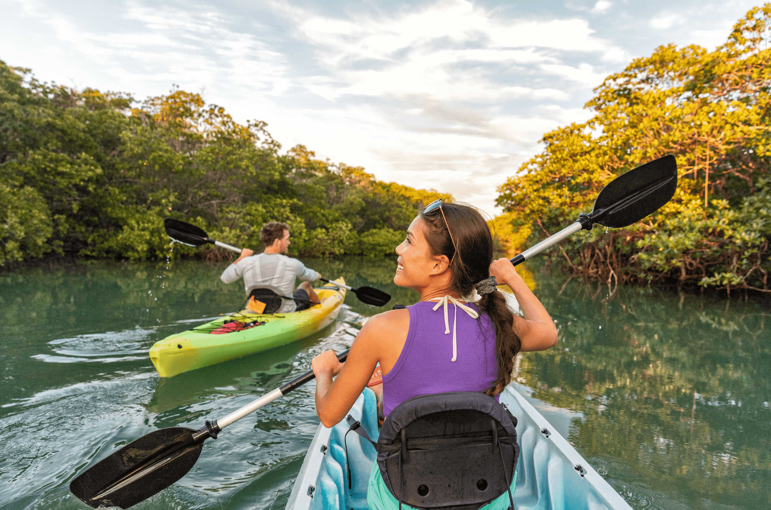 Kayakers paddling through mangrove-lined river at sunset