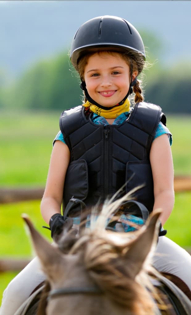 Young rider on horse in protective vest on grassy coastal trail