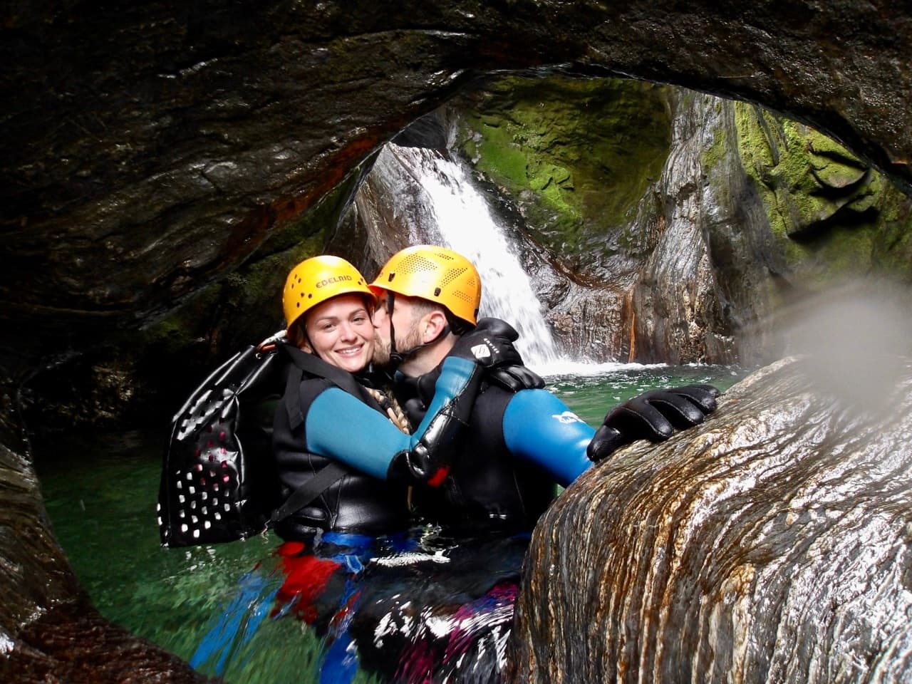 Couple canyoning in waterfall pool beneath rocky overhang New Zealand
