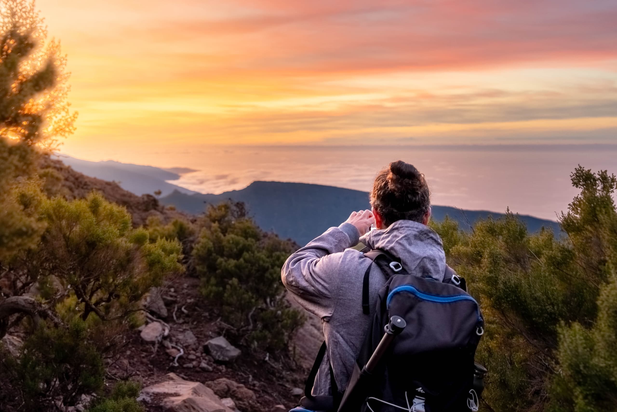 Backpacker photographing sunset over mountainous coastal views