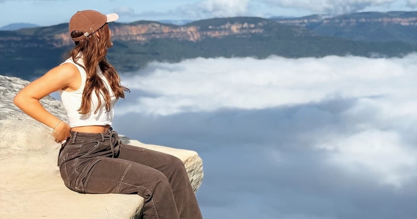 Hiker sitting on cliff edge above clouds with valley view