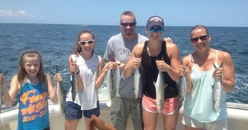 Family anglers holding catches on boat during coastal fishing charter