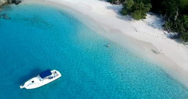 Motorboat anchored off white-sand tropical beach, aerial view